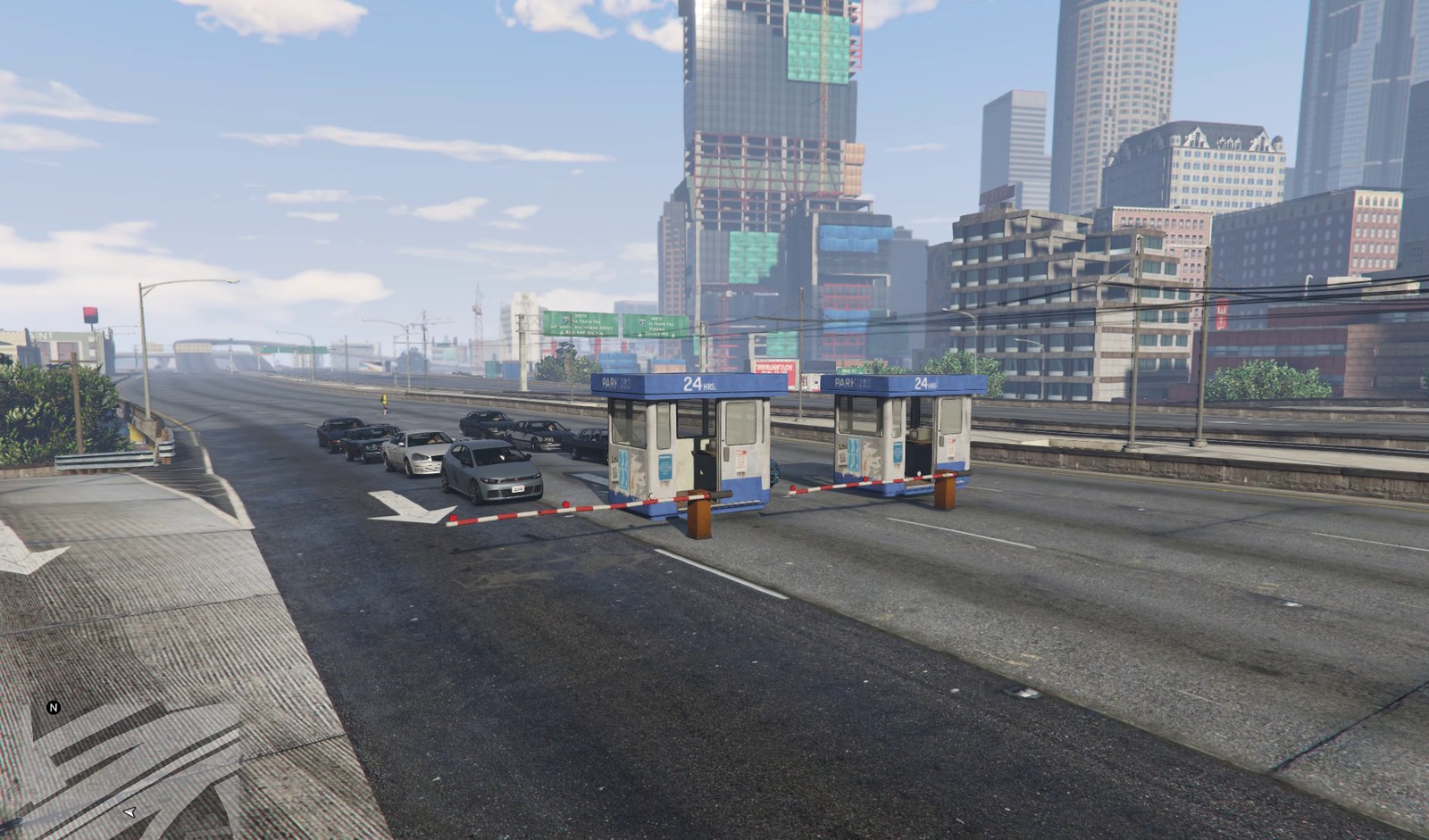 Traffic queued at the closed toll plaza: a fuel tanker, a pickup and several cars stopped in a line behind the barrier arms.